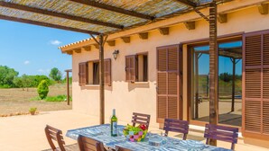 Un patio coperto con un tavolo apparecchiato per mangiare, una bottiglia di vino e una ciotola di frutta.