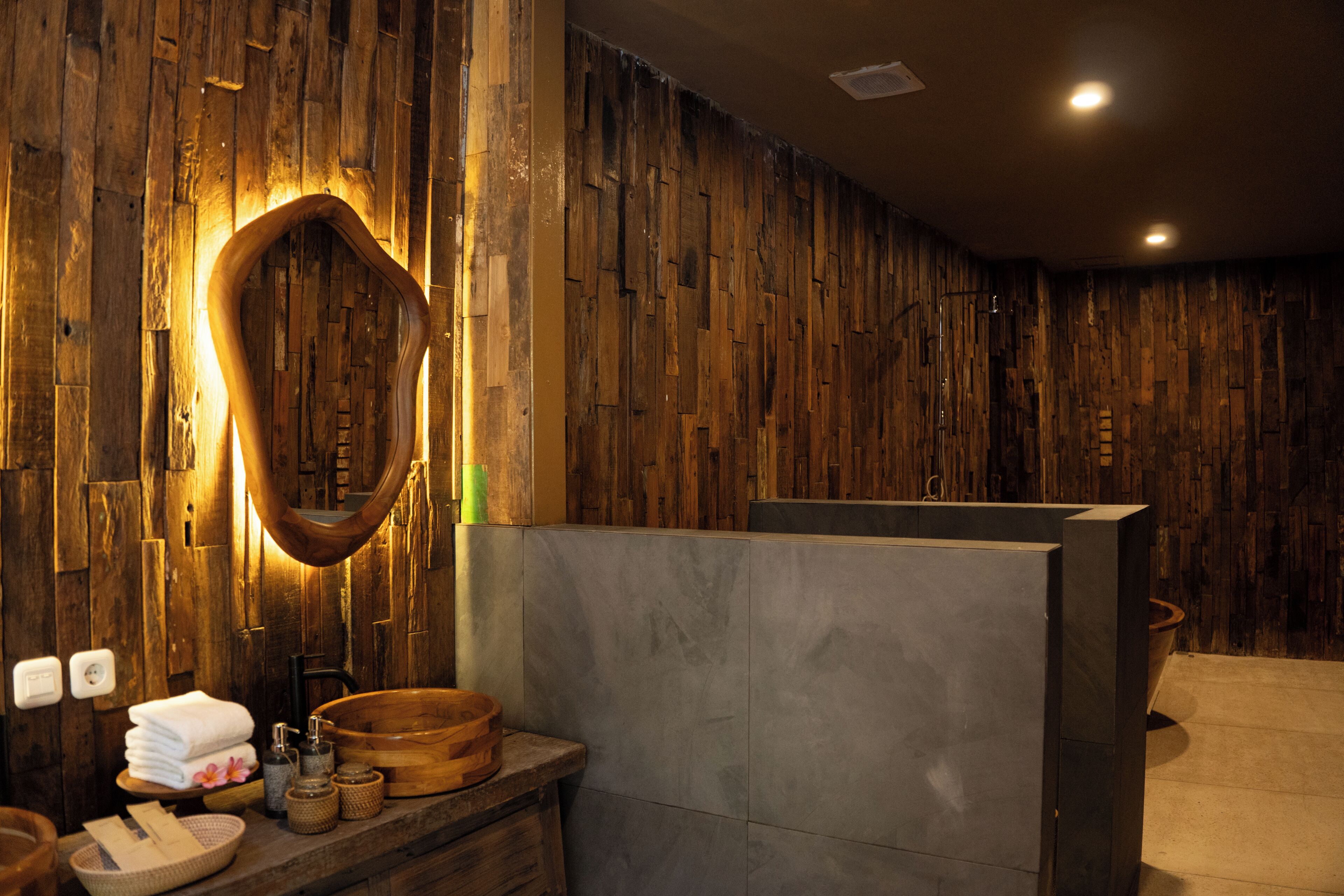 A bathroom with a wooden wall, a large mirror, a sink, and a towel rack.