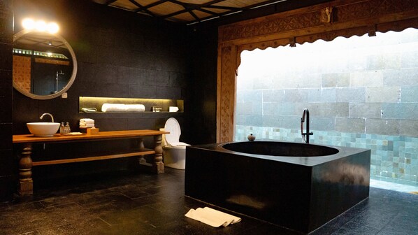 A modern bathroom with a freestanding bathtub, a wooden vanity, a round mirror, and a tiled wall. - Seaside Oceana Resort by Mahaprana (Kubutambahan)