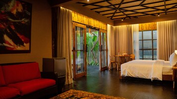 Habitación de hotel con cama, sofá rojo, una mesita y un ventanal con cortinas.