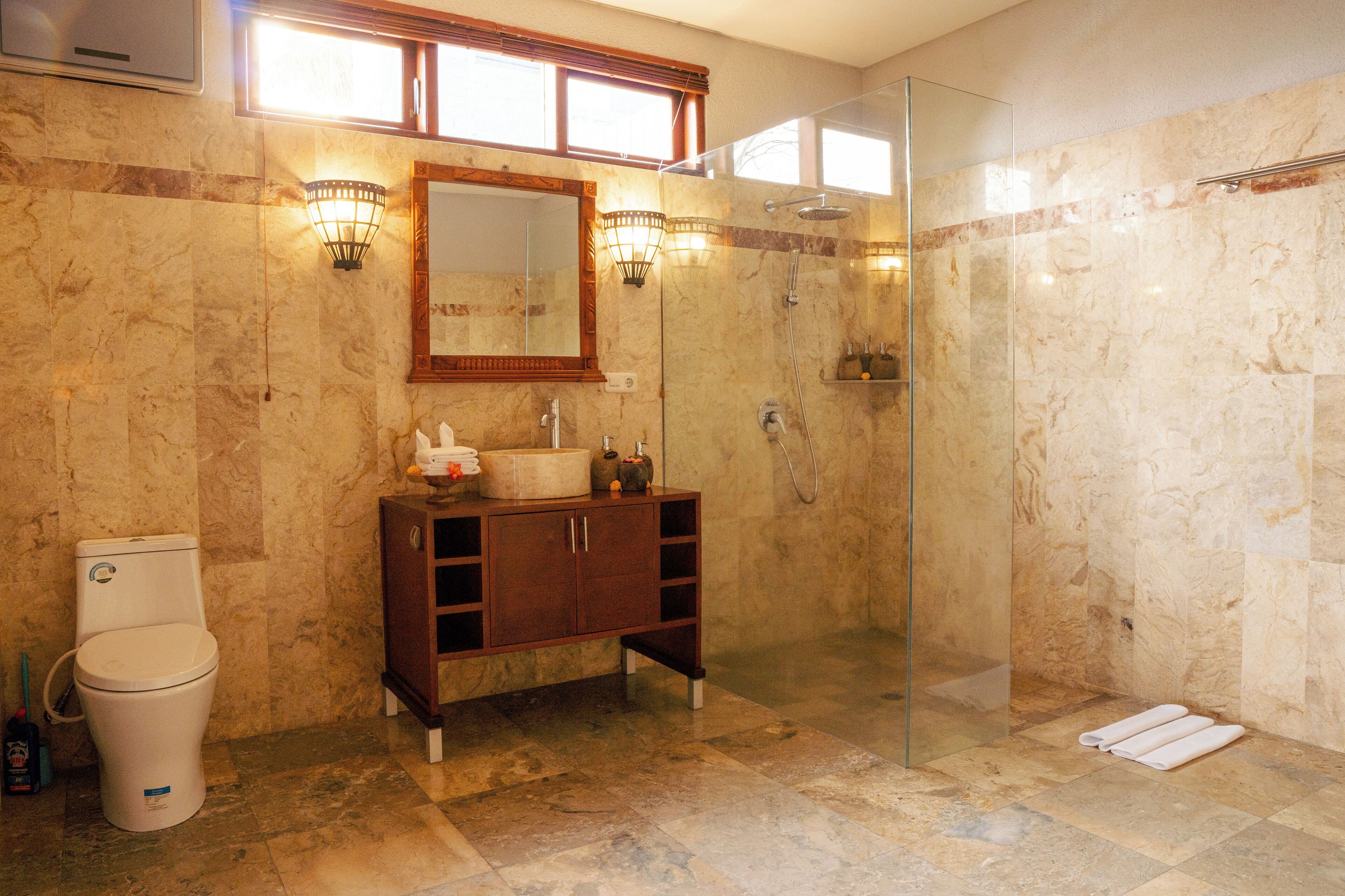 Un baño con piso de mármol, tocador de madera, cabina de ducha de vidrio y un inodoro.