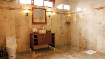 Un baño con piso de mármol, tocador de madera, cabina de ducha de vidrio y un inodoro.