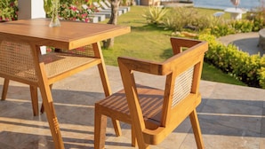 Een houten tafel met stoelen buiten, met uitzicht op de zee en palmbomen.