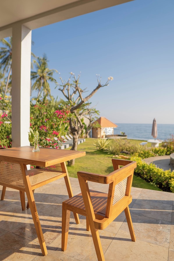 A wooden table and chair set outdoors with a view of the sea and palm trees. - Seaside Oceana Resort by Mahaprana (Kubutambahan)