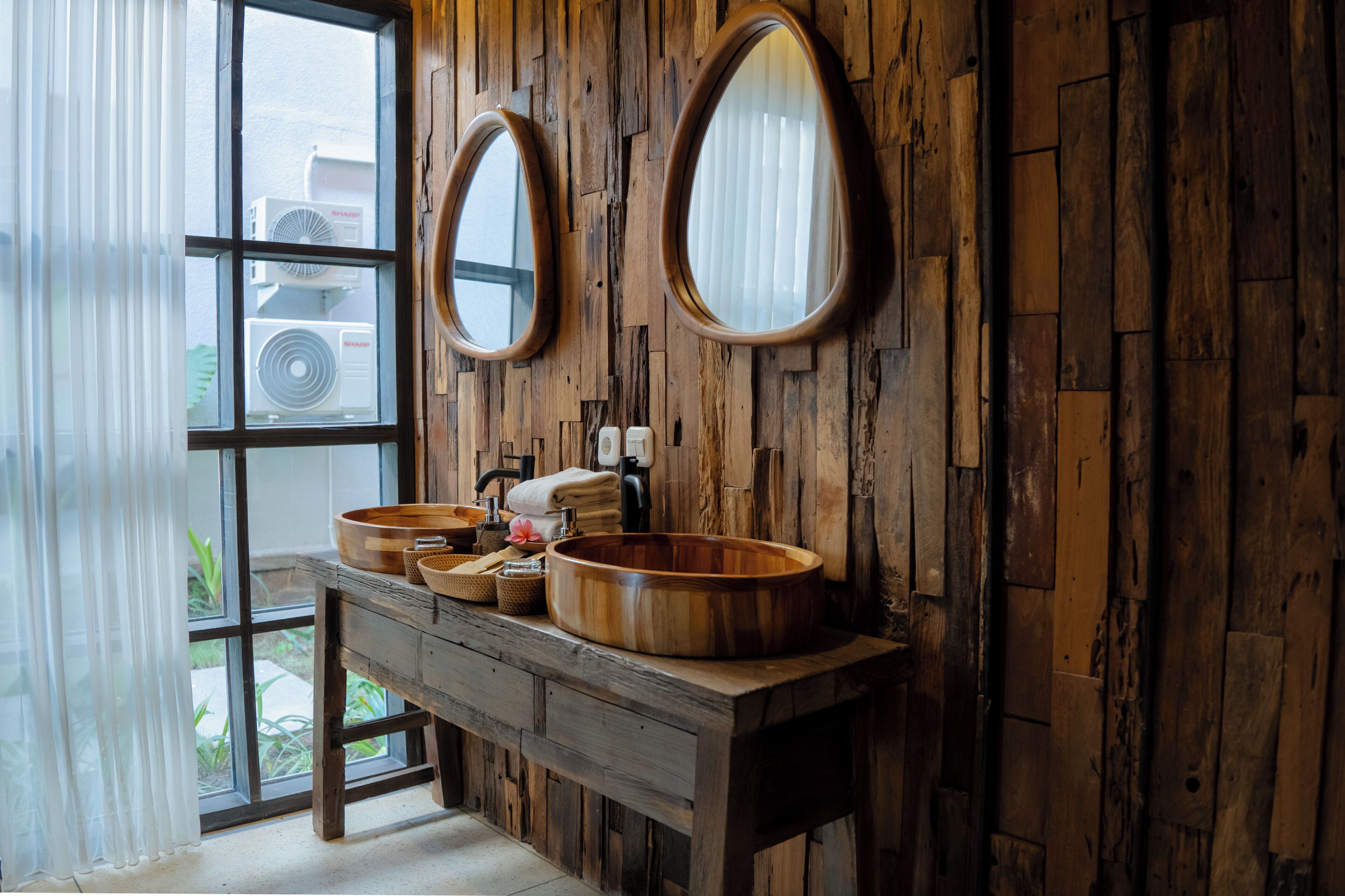 A rustic bathroom with wooden walls, two oval mirrors, and a wooden vanity with two sinks.
