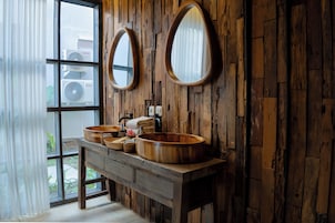 Un baño rústico con paredes de madera, dos espejos ovalados y un tocador de madera con dos lavamanos.