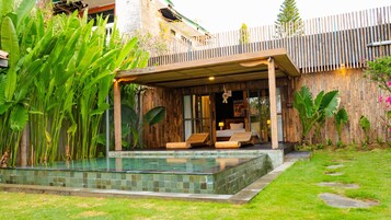 Una villa moderna con piscina, terraza de madera y exuberante vegetación.