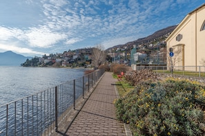 A waterfront promenade with a paved walkway, a metal railing, and a building with a yellow facade. - Pianello Charming Lake View (Pianello del Lario)