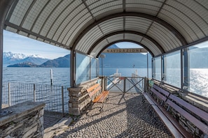 A covered viewing area with stone benches and a railing overlooking a body of water with mountains in the background. - Pianello Charming Lake View (Pianello del Lario)