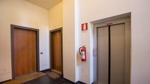 A hallway with two wooden doors, a fire extinguisher mounted on the wall, and an elevator with a sign indicating it is not in use. - Casa Daniele in Menaggio (Menaggio)