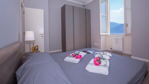 A hotel room with two beds, a large wardrobe, a window with a view, and a bedside table with a lamp. - Casa Daniele in Menaggio (Menaggio)
