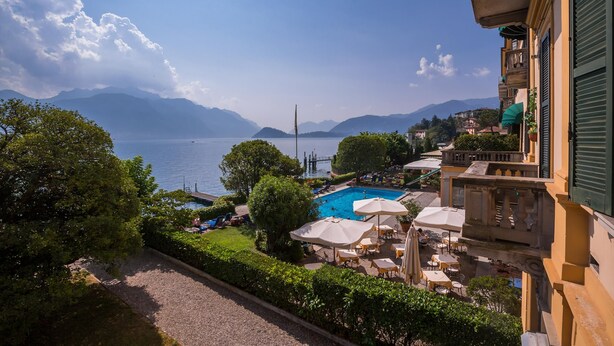 A view of a pool area with lounge chairs and umbrellas, surrounded by greenery and overlooking a lake with mountains in the background. - Casa Daniele in Menaggio (Menaggio)