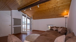A spacious room with a large bed, wooden ceiling beams, a radiator, and a view through a glass door. - Villa Patricia in Acquaseria (San Siro)