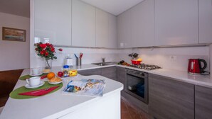 A modern kitchen with white cabinets, a gas stove, a sink, and a red kettle. - Villa Patricia in Acquaseria (San Siro)
