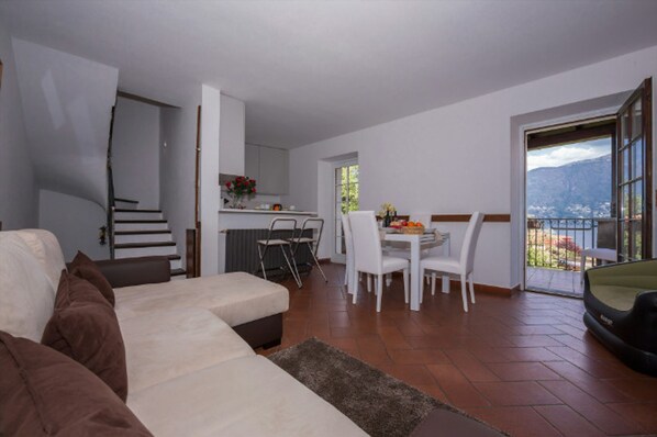 Una sala de estar con un sofá, un comedor con mesa y sillas, una cocina y un balcón con vistas a las montañas.