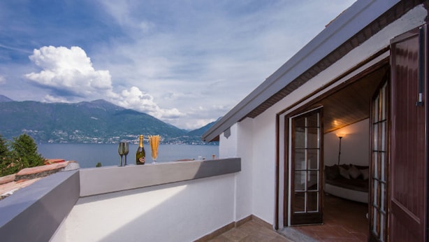 A balcony with a view of a lake and mountains, a wine bottle, and a glass of wine. - Villa Patricia in Acquaseria (San Siro)