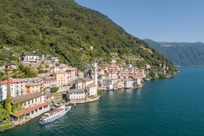 A coastal town with buildings along the water, a boat docked at the pier, and a mountainous backdrop. - Menaggio 57 in Menaggio (Menaggio)
