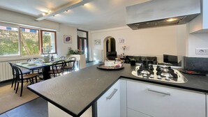 Une cuisine moderne dotée d’un îlot central, d’un coin repas avec une table et des chaises, et offrant une vue sur l’extérieur grâce à de grandes fenêtres.