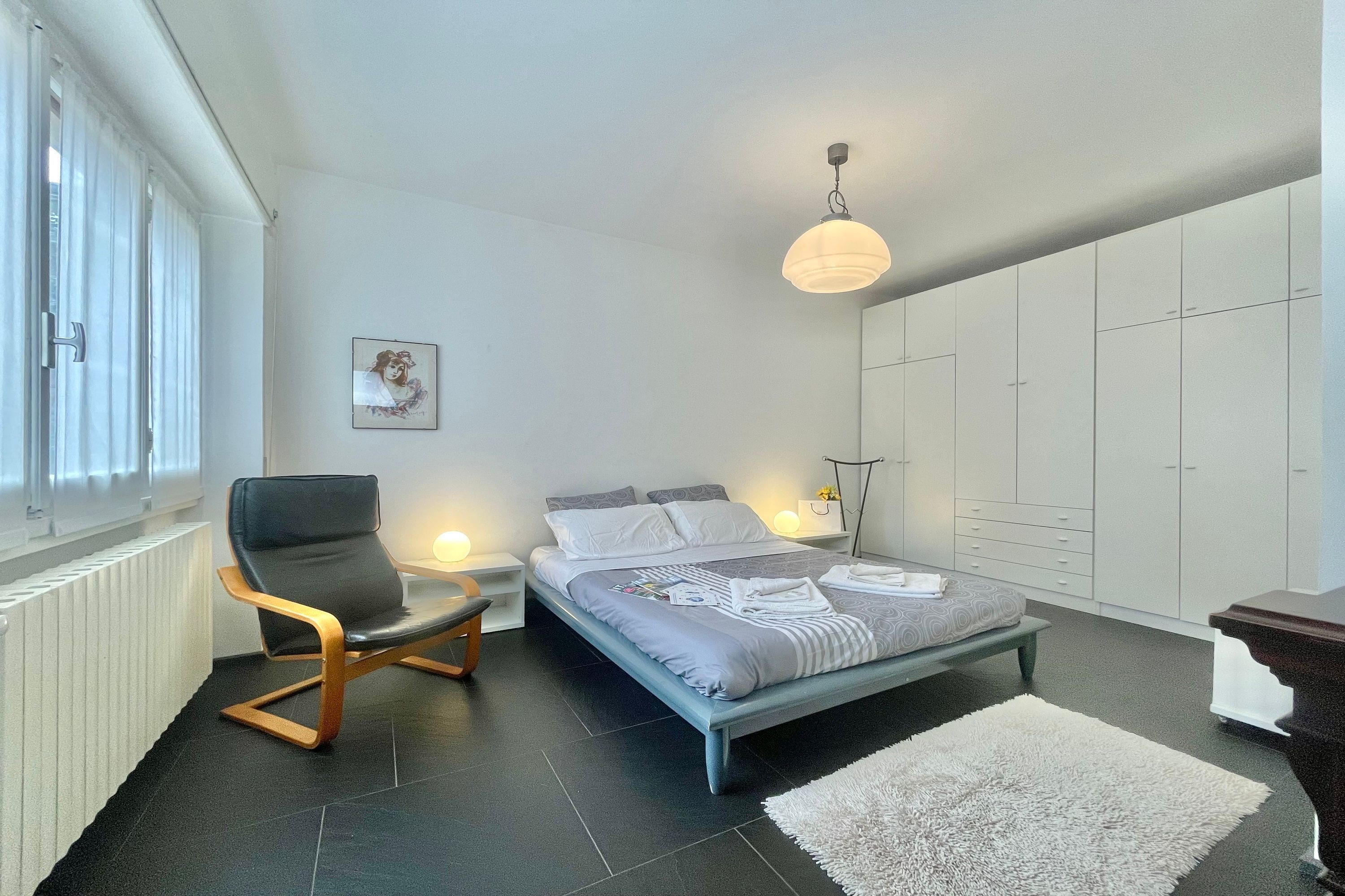 Ein modernes Schlafzimmer mit Bett, Sessel, Nachttisch, Lampe und Kleiderschrank.