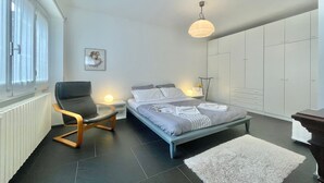 Une chambre à coucher moderne comprenant un lit, une chaise, une table de chevet, une lampe et une armoire.
