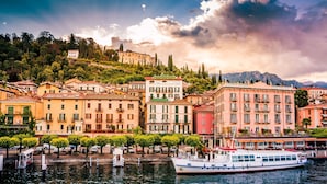 Un hôtel situé au bord de l’eau, avec un bateau amarré devant, entouré de bâtiments colorés et d’arbres.