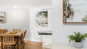 A dining area with a wooden table and chairs, a small side table with a candle, and two large abstract paintings on the wall.