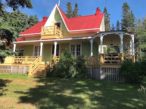 A two-story house with a red roof, a porch with a wooden railing, and a fenced yard.