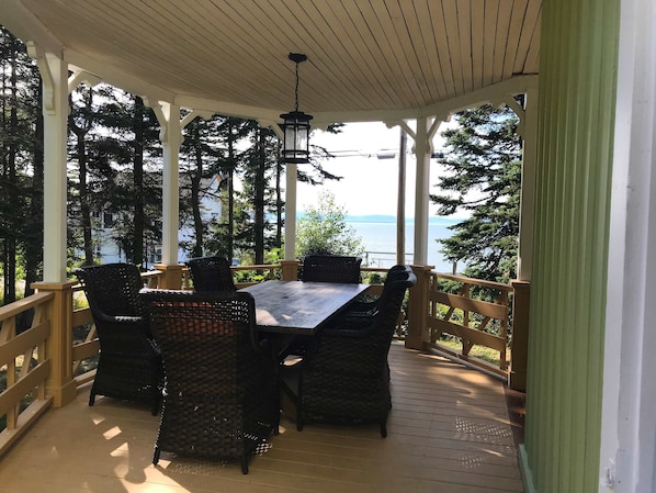 A covered outdoor seating area with a table and chairs, overlooking a body of water.