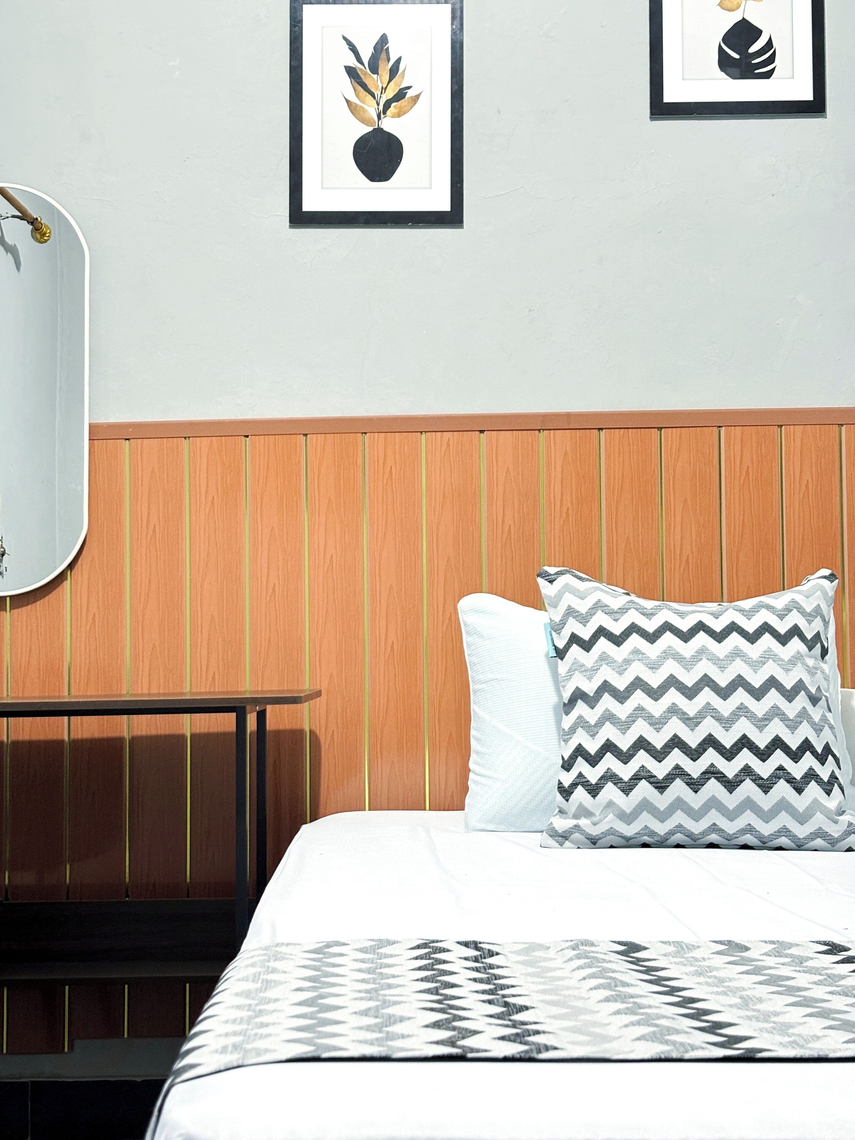A hotel room with a wooden headboard, a bed with patterned bedding, a bedside table, and two framed wall art pieces.