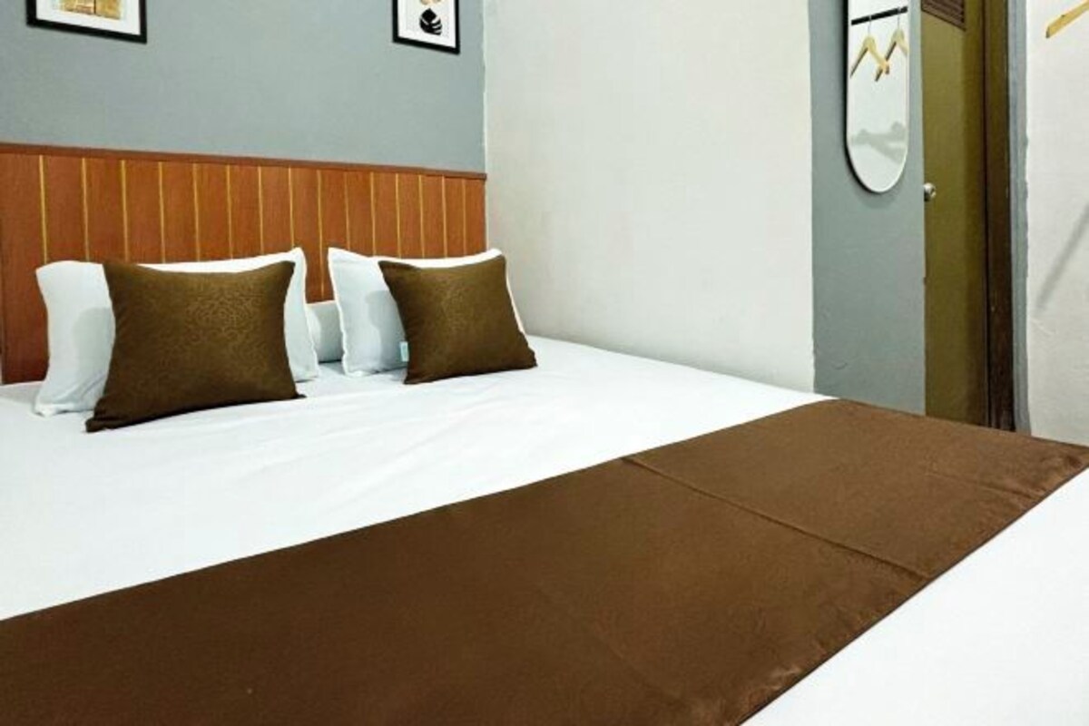 Una habitación de hotel con cama, almohadas, cabecera, espejo y puerta.