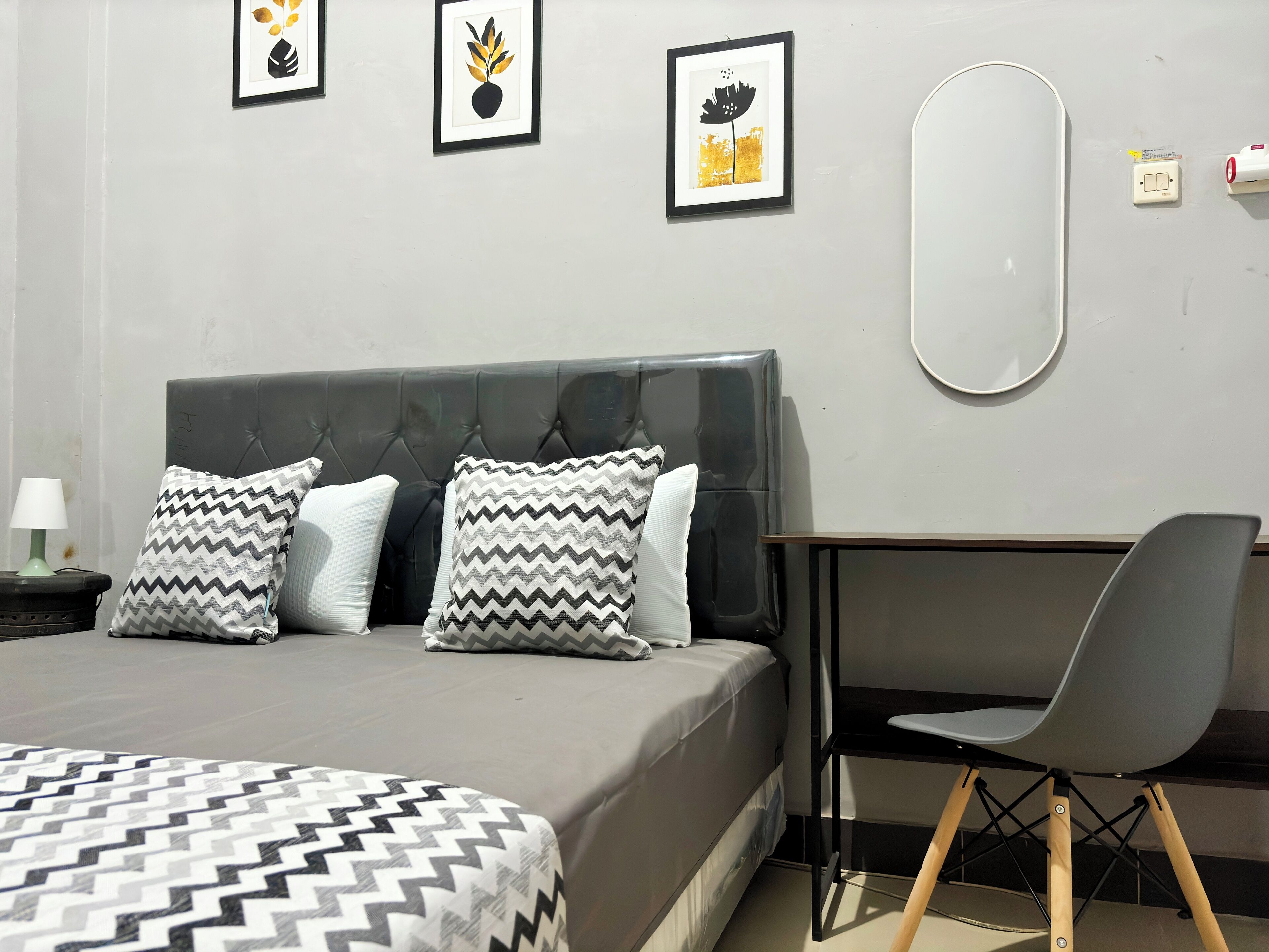 A bedroom with a bed, a desk, and a chair. There are three framed pictures on the wall.