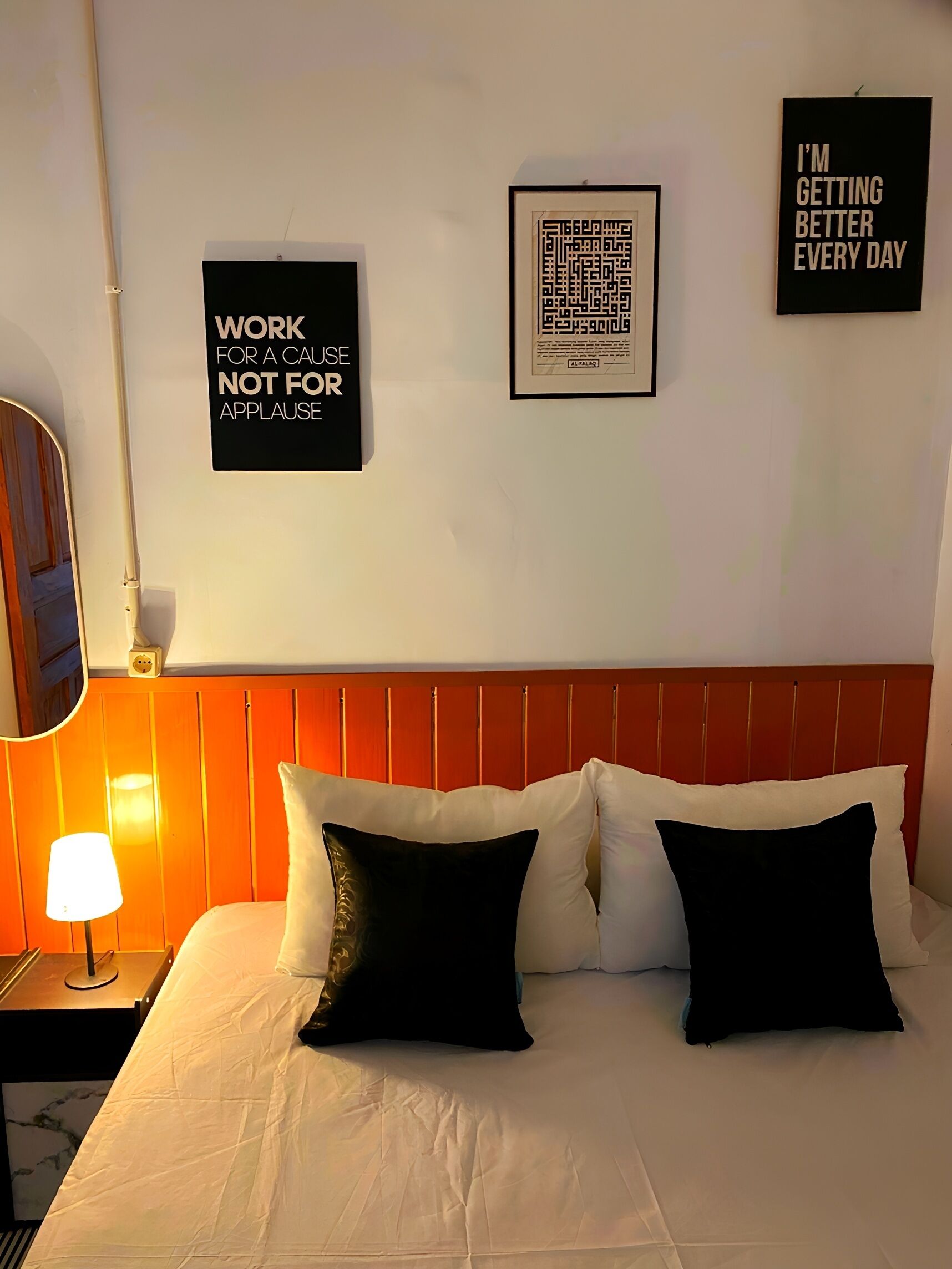 A hotel room with a bed, a nightstand, a lamp, and motivational posters on the wall.