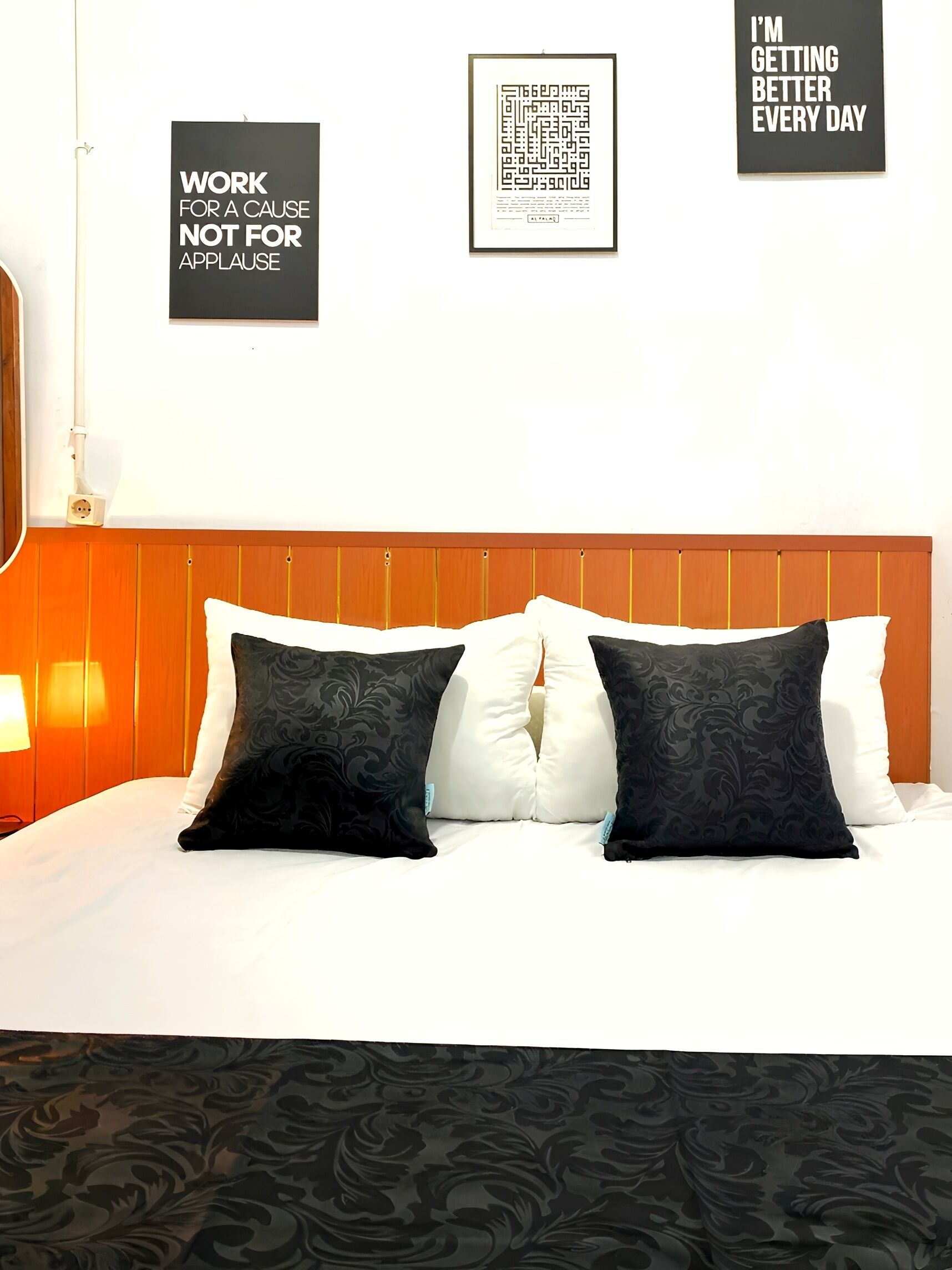 Une chambre d’hôtel avec une tête de lit en bois, du linge de lit blanc et des coussins décoratifs. Des affiches motivantes sont accrochées au mur.