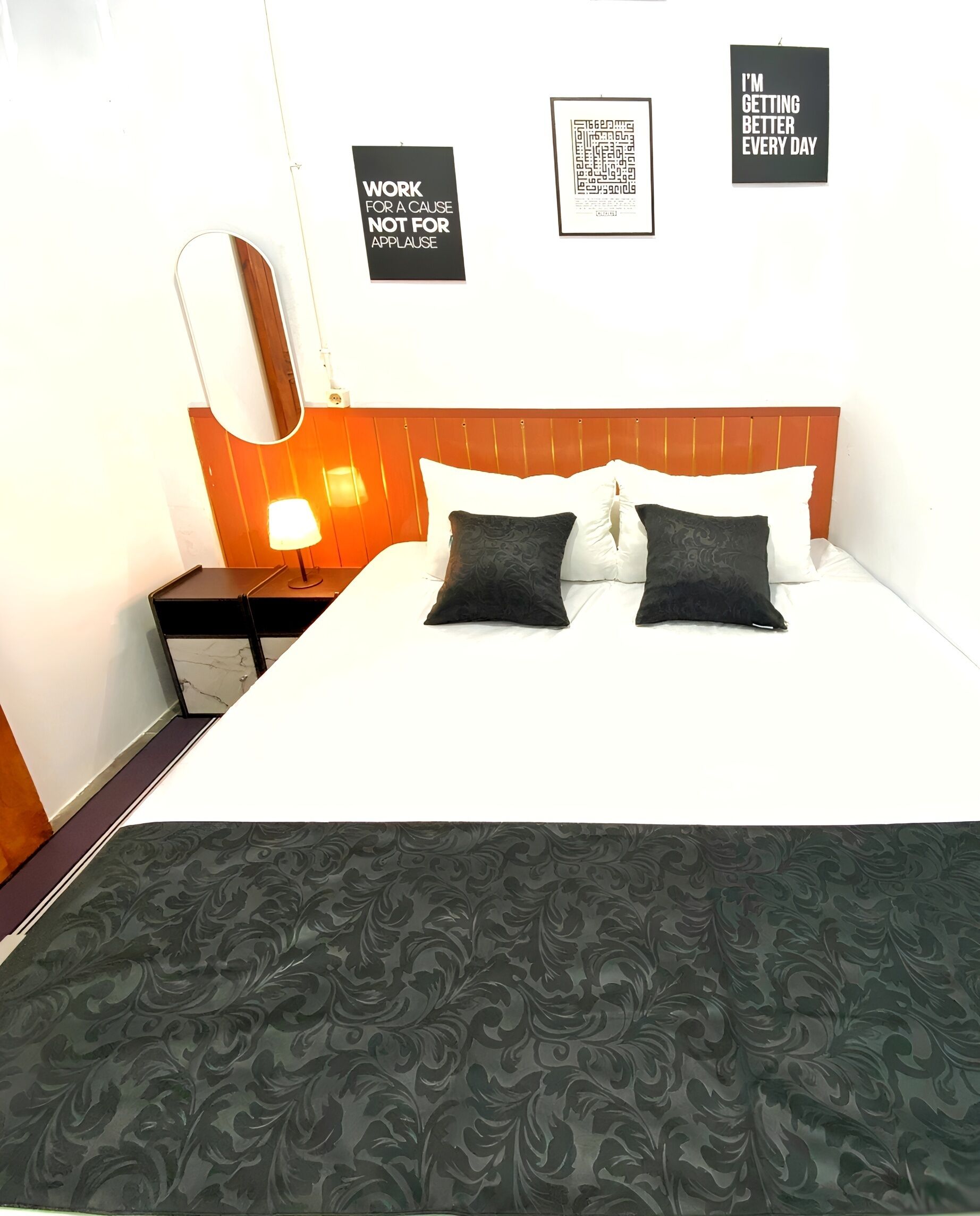 Een hotelkamer met een bed, een nachtkastje, een lamp en drie motiverende posters aan de muur.