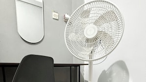 A room with a standing fan, a chair, a mirror, and a wall socket. - JOGJA DAY INN (Yogyakarta)