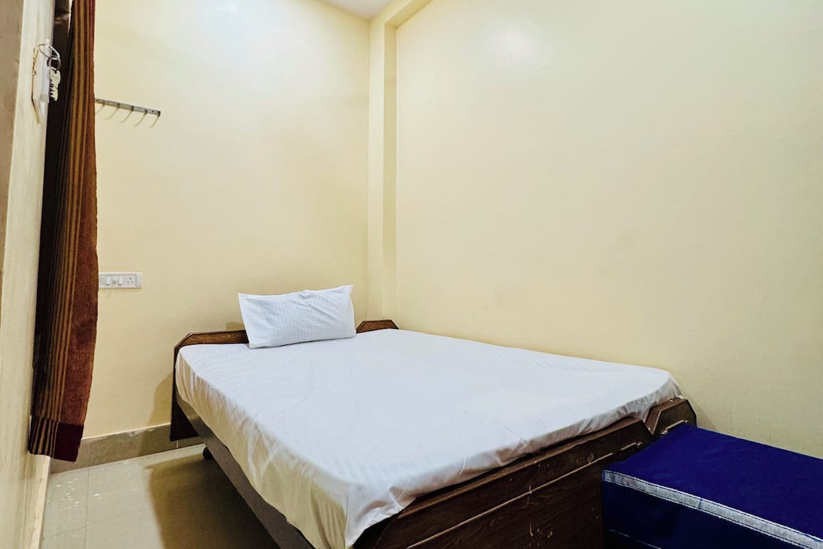 Una habitación pequeña con cama individual, ventilador de techo, estructura de cama de madera y un baúl azul.