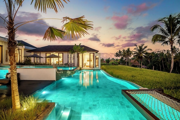 A modern resort with a swimming pool, palm trees, and a sunset view.