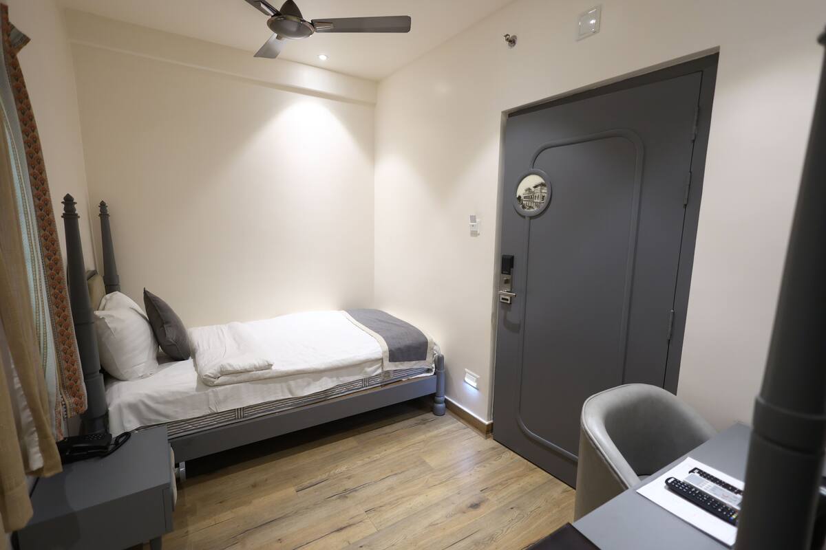 A bedroom with a bed, a desk, a chair, a door, and a ceiling fan.