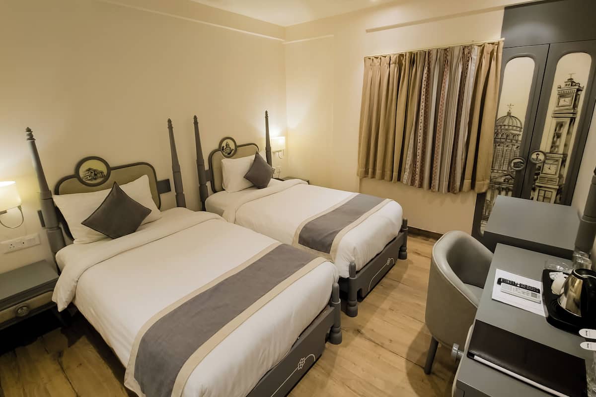 A hotel room with two beds, a desk, and a mirror reflecting a building.