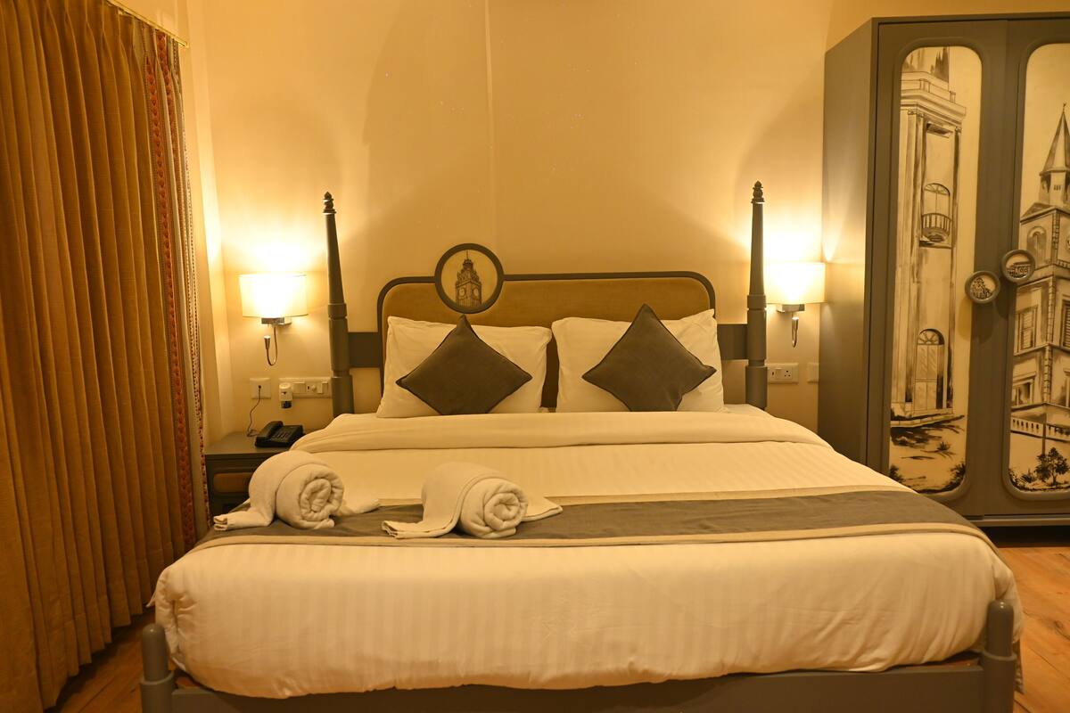 A hotel room with a neatly made bed, two bedside lamps, a telephone, and a wall with a mural.