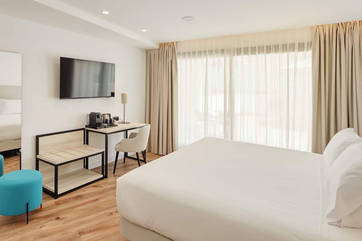 Habitación de hotel con una cama grande, un escritorio con silla, televisión y ventana con cortinas.