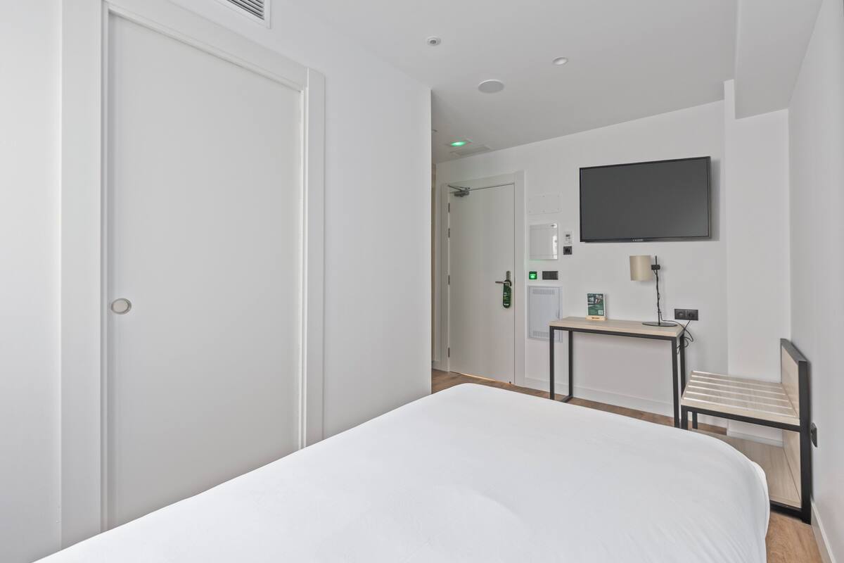A hotel room with a bed, a desk, a chair, a TV, and a door.