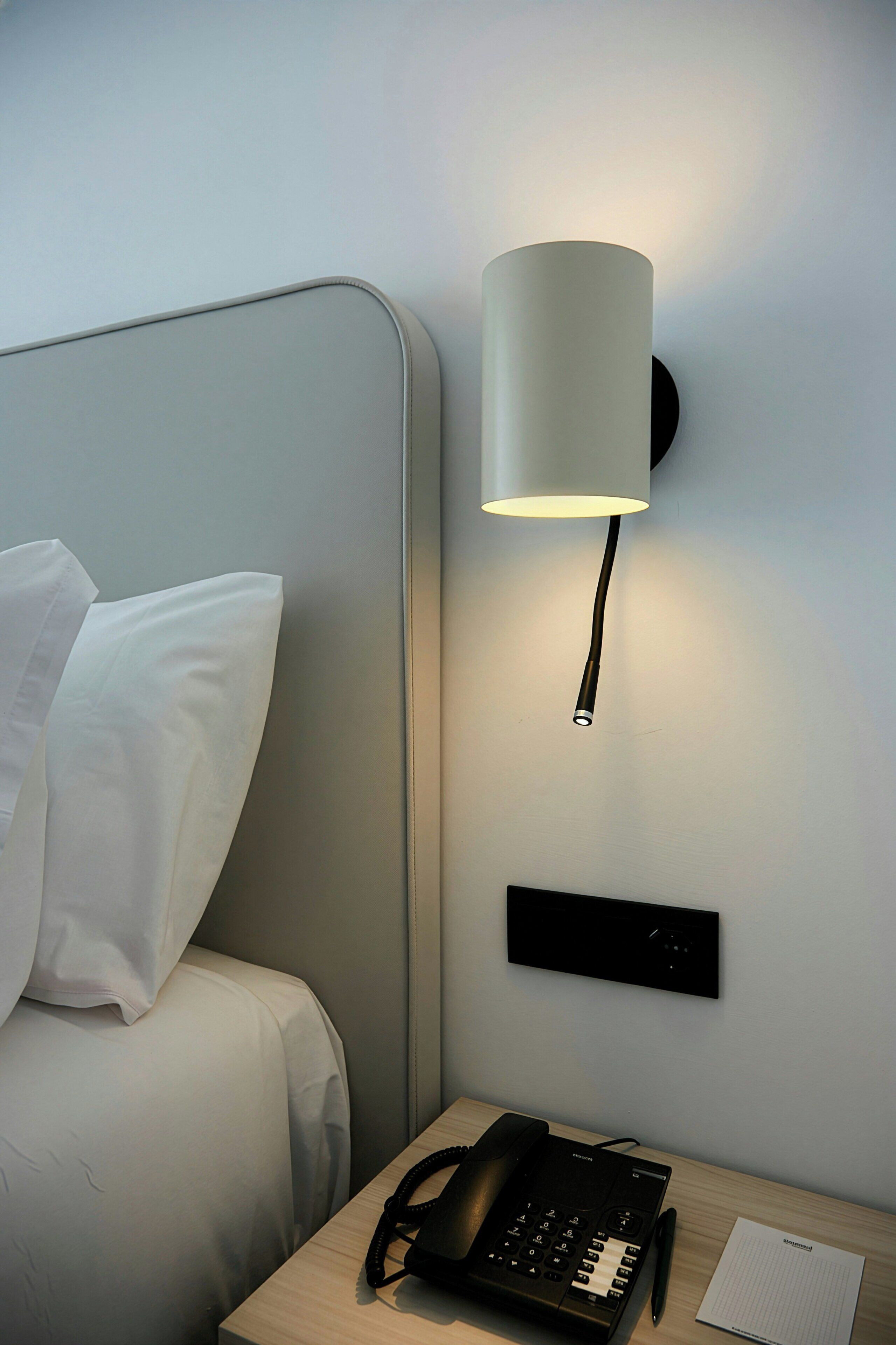 A hotel room with a bed, a bedside lamp, a telephone, and a nightstand.