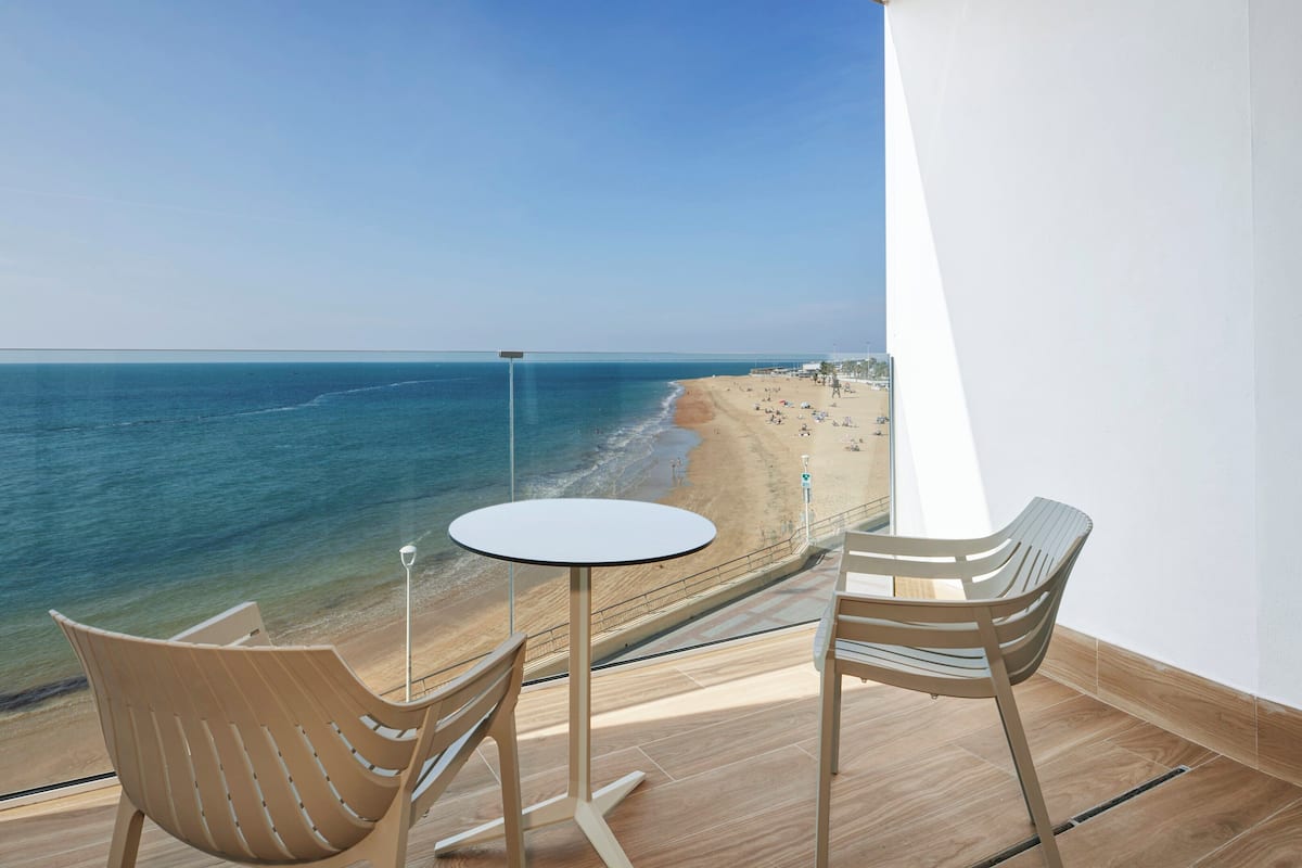 Un balcón con vista a la playa, una mesa redonda, dos sillas y una lámpara.