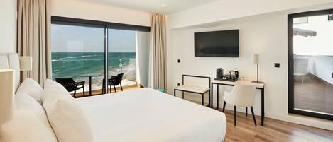 A hotel room with a large bed, a desk with a chair, a TV, and a view of the ocean.