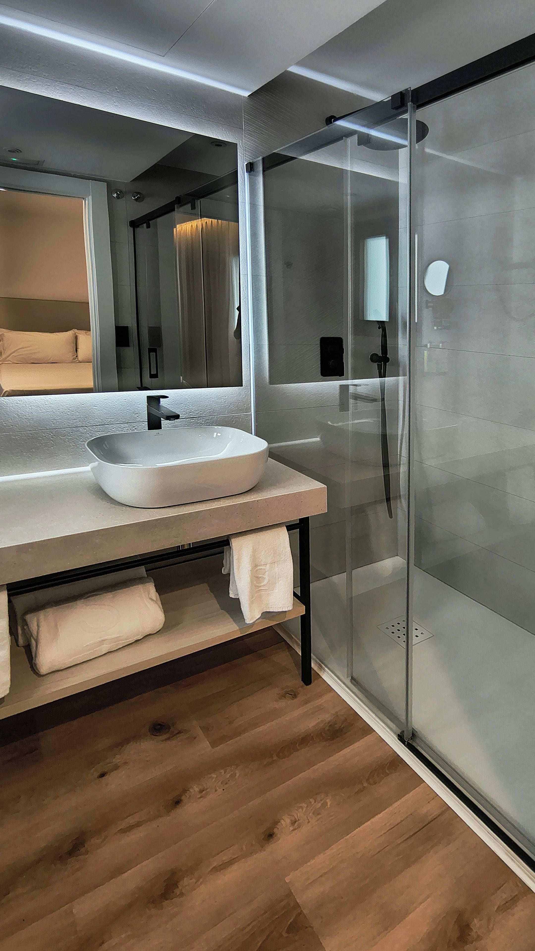 A modern bathroom with a glass shower enclosure, a large mirror, and a white sink.