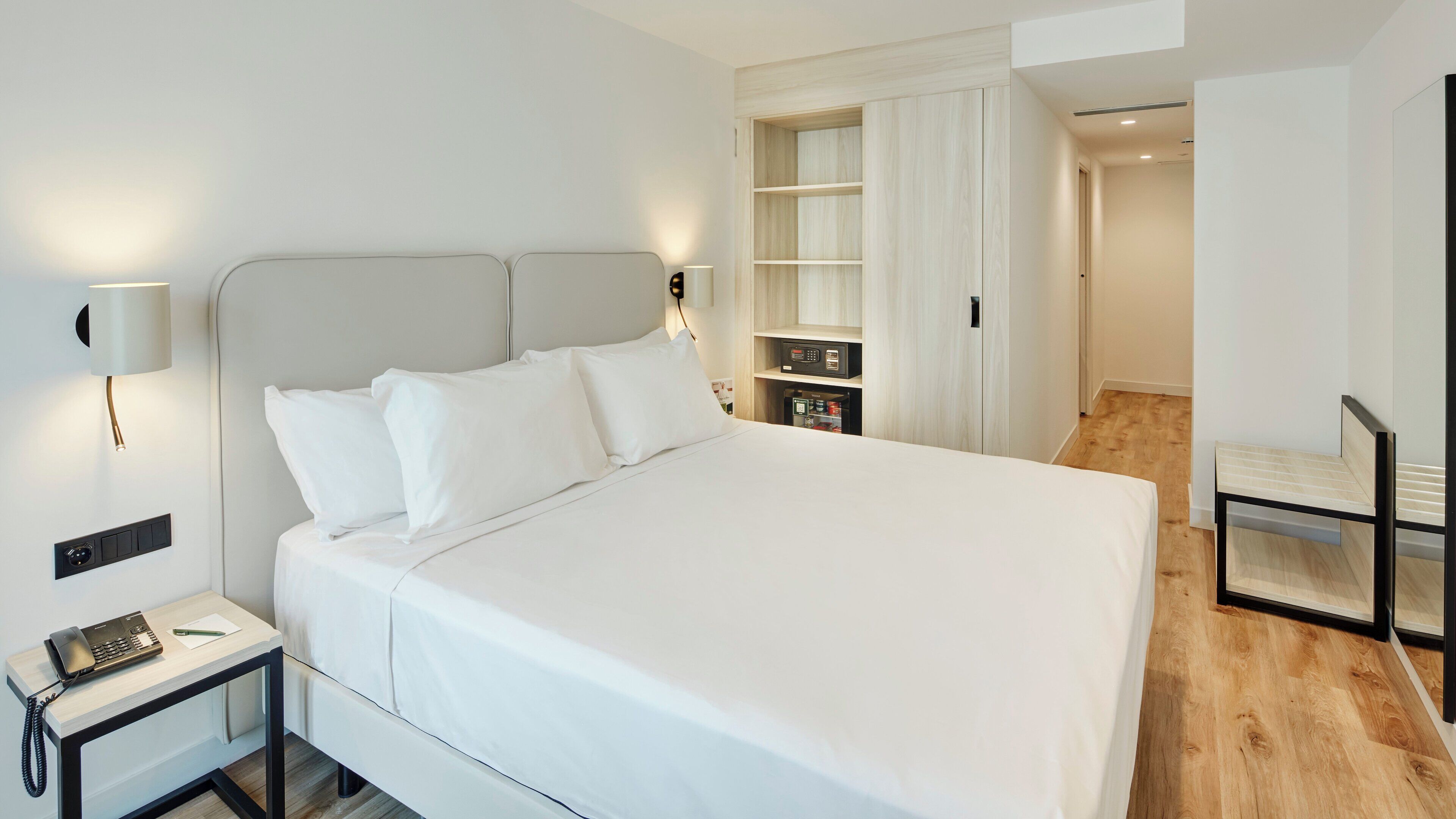 Ett modernt hotellrum med en stor säng, sänglampor, ett skrivbord med en telefon och en garderob med en spegel.