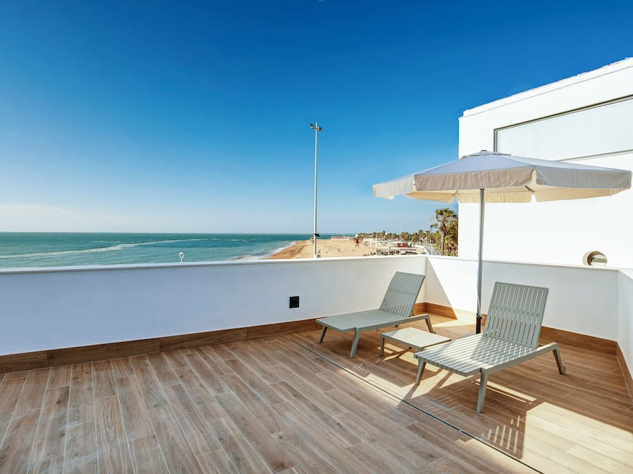 A balcony with a view of the beach, two lounge chairs, and a large umbrella.
