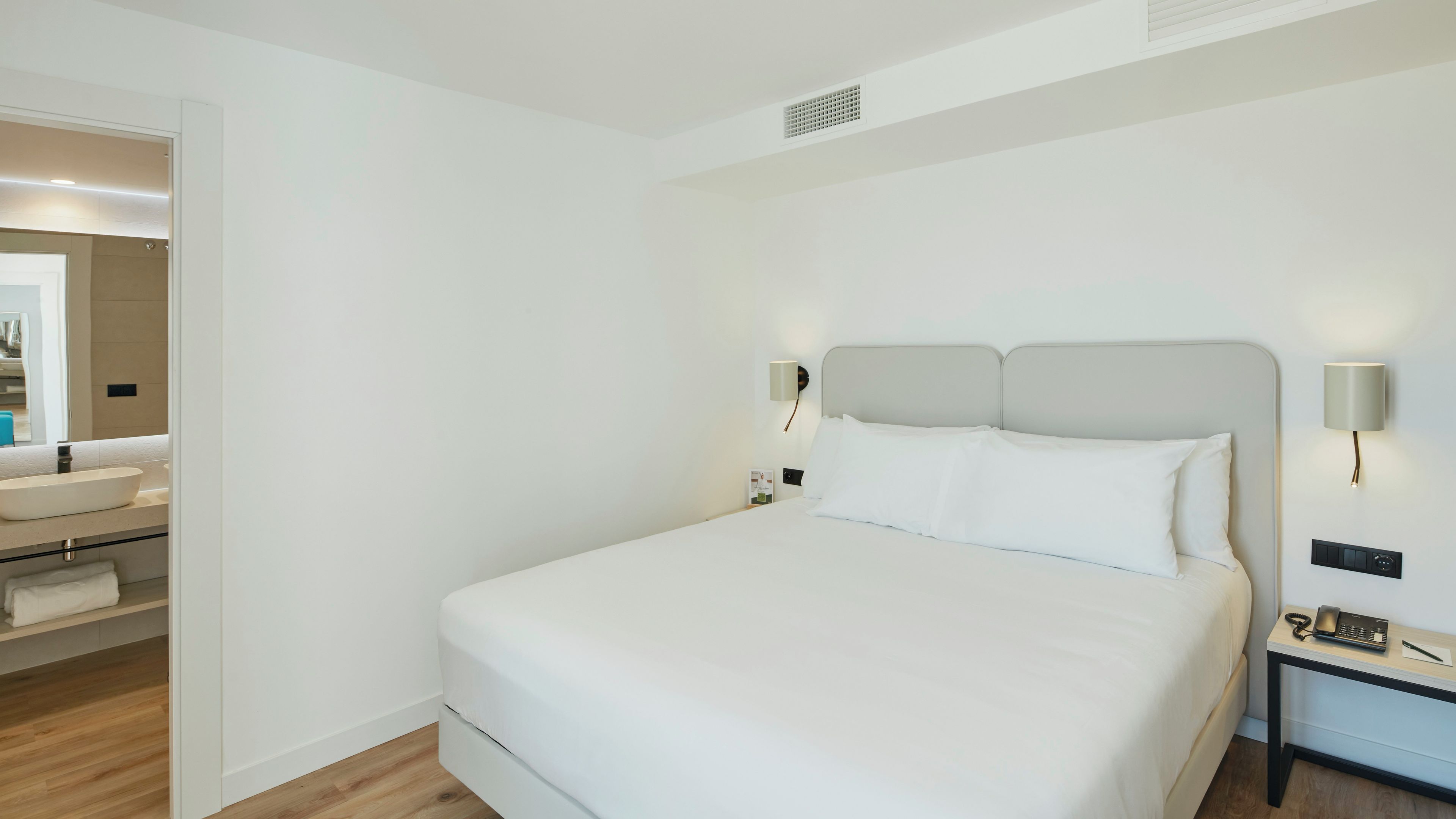 A hotel room with a bed, bedside table, and a bathroom visible through an open door.