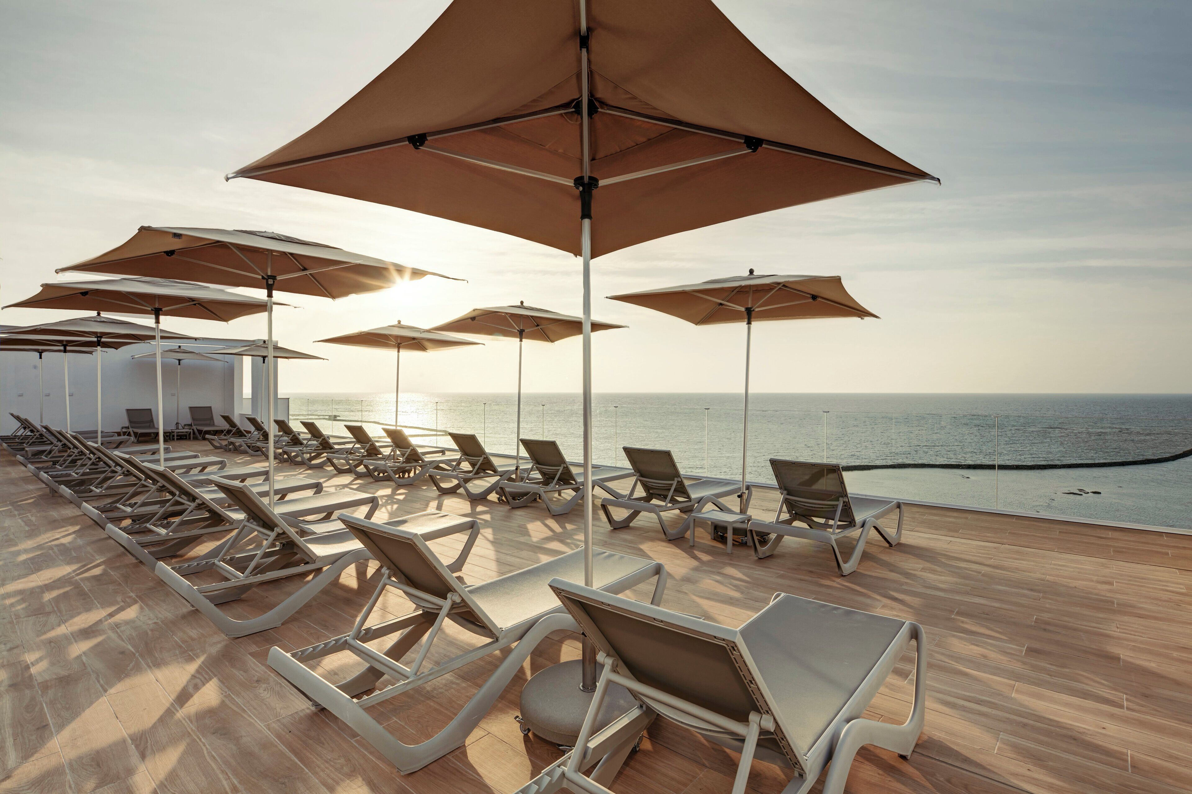 Terraza soleada con sillones de descanso y sombrillas, con vistas al mar.